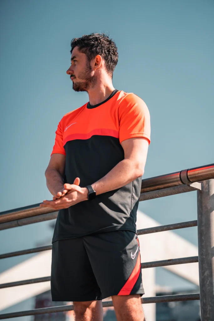 Homem com camiseta esportiva laranja e preta e bermuda preta