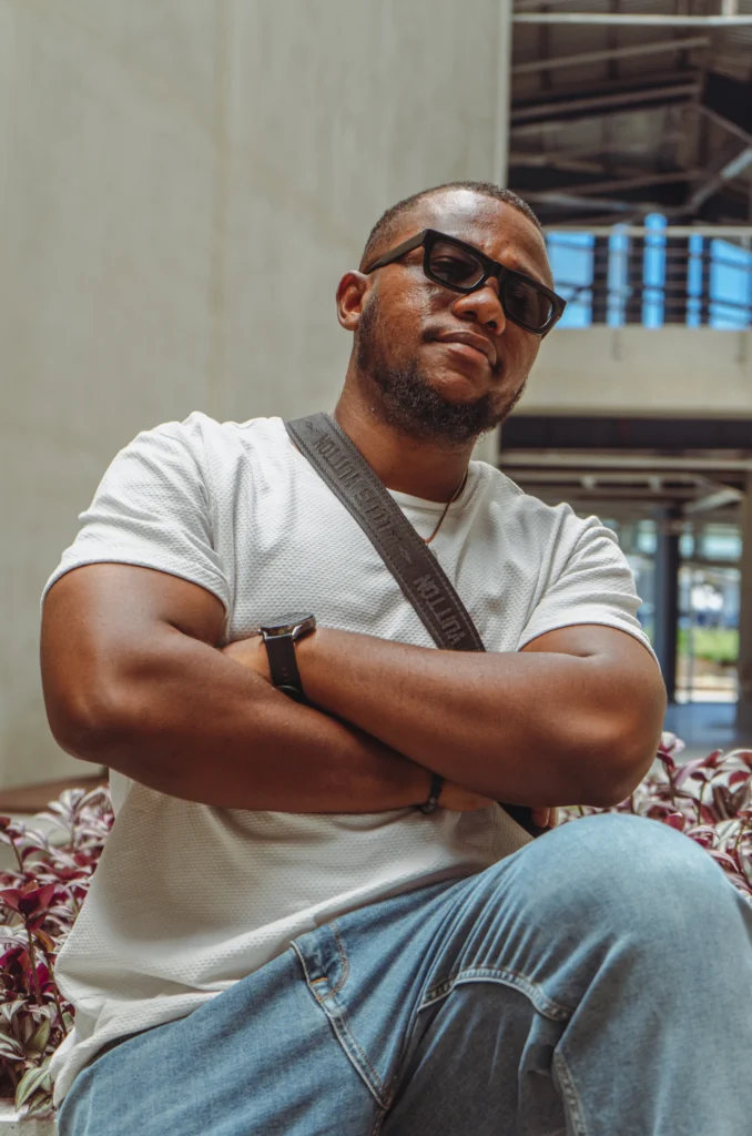 Homem de camiseta clara e calça jeans sentado com os braços cruzados
